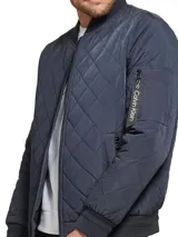 Campera estilo bomber acolchada de color azul marino, con patrón de costuras en rombos. Presenta cierre frontal de cremallera, cuello, puños y dobladillo en punto canalé oscuro. Incluye bolsillo utilitario con cremallera en la manga izquierda con cinta con el logo de Calvin Klein.
