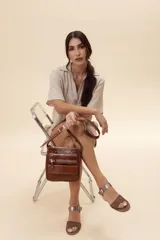Sandalia de cuero marrón con tira frontal en cuero y correa al tobillo metalizada con hebilla ajustable. Cuenta con tacón ancho y bajo de acabado símil madera.