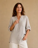 Camisa de lino color beige, de corte holgado, con cuello mao, bolsillos frontales en el pecho, mangas largas remangables y cierre frontal con botones.