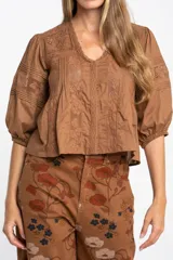 Blusa de algodón color marrón con cuello en V, mangas tres cuartos con puños elásticos y detalles de encaje y alforzas en el frente.