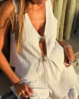 Blusa sin mangas color blanco, tejida con textura acanalada y escote pronunciado en V, sujeta en el centro con dos apliques metálicos con forma de sol.