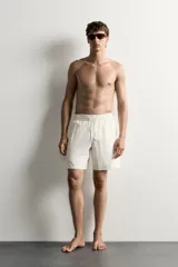 Short de baño largo en color beige, confeccionado en tejido técnico con tacto aterciopelado. Cuenta con cintura elástica ajustable con cordón, bolsillos laterales y detalle de bolsillo trasero, además de forro interior.