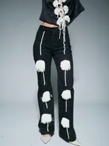 Pantalón de tiro alto color negro, con corte recto y apliques decorativos de cordones blancos terminados en borlas de flecos.