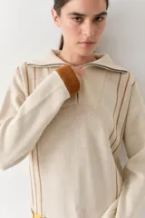 Buzo de punto color beige con rayas verticales marrones, cuello polo con cierre frontal, puños y ruedo acanalados en color marrón. Incluye cordones amarillos ajustables en la cintura.