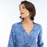 Camisa azul con estampado floral en blanco, de corte oversize, mangas tres cuartos, escote en V con cuello y detalle de nudo en el frente.