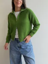 Cardigan tejido de color verde, con cierre frontal de doble vía, cuello alto y mangas largas. Presenta terminaciones en rib en puños y cintura, con un diseño versátil y moderno.