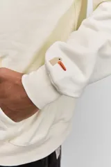 Buzo con capucha de corte holgado, color crema, con bolsillo frontal tipo canguro y pequeña estampa tipográfica en el pecho.