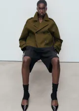 Chaqueta corta de doble botonadura en color verde militar, con cuello de solapa, bolsillos laterales, trabillas en los hombros y mangas largas con puños abotonados.