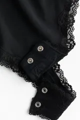 Body negro de punto suave con ribetes de encaje en escote y cavado. Presenta escote en V, breteles ajustables y copas forradas con relleno extraíble. Tiene un refuerzo interior y corte alto en la parte trasera. Diseño sin costuras visibles.