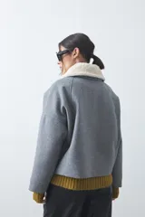 Campera corta de paño color gris con cuello de corderito blanco, cierre frontal con botones y bolsillos laterales.