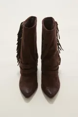 Bota corta de gamuza color chocolate, con punta fina y taco bajo. Presenta detalle de flecos en el lateral exterior y dos correas decorativas con hebillas metálicas en el tobillo.