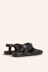 Sandalia de cuero negro estilo huarache, con puntera cerrada mediante tiras finas entretejidas a mano, tira ajustable al tobillo con hebilla metálica y suela plana con taco de 1 cm.
