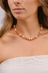 Gargantilla multipiezas confeccionada con una combinación de cristales facetados, cuentas de piedra natural en tonos naranjas y salmón, y pequeñas esferas metálicas. Cuenta con cierre de acero.