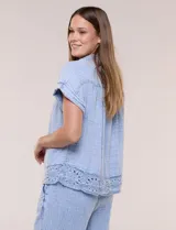 Blusa de algodón celeste con textura tramada tipo denim lavado, cuello solapa abierto en V, botones frontales y detalle de puntilla tejida al crochet en el ruedo.