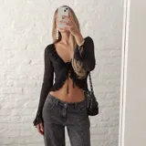 Blusa corta negra transparente de manga larga, con escote en V profundo adornado con volados y cierre frontal con tiras para atar.