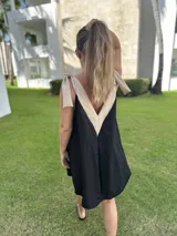 Vestido corto color beige, con escote en V con borde blanco, breteles anchos con lazos y corte holgado.