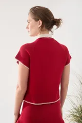 Top tejido de punto color rojo con cuello polo blanco, medio cierre frontal y detalles de costuras visibles en contraste en los bordes de las mangas y el ruedo.