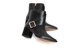 Bota corta de cuero color negro con textura efecto piel de serpiente, punta fina y tacón cuadrado medio. Presenta una tira cruzada sobre el empeine con una hebilla metálica dorada cuadrada en el lateral.