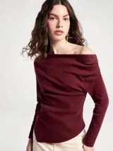 Blusa negra de manga larga con diseño asimétrico en el escote, dejando un hombro al descubierto. Presenta un corte ajustado con detalle de frunces laterales que crean un efecto drapeado en el torso.