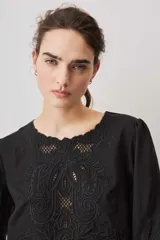 Blusa negra con detalles de apliques bordados en el pecho y las mangas, cuello redondo y mangas largas abullonadas.
