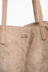 Bolso tipo tote de gran tamaño confeccionado en gamuza sintética color tostado. Presenta un diseño minimalista con asas largas de hombro y una pequeña placa metálica frontal con el logo de la marca.