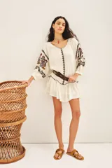 Vestido corto de bambula color celeste, con escote redondo, mangas tres cuartos abullonadas y falda con volado en el ruedo. Presenta bordados decorativos en el frente y las mangas, y cuenta con un cinturón de la misma tela para ajustar a la cintura.