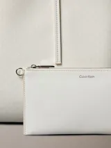 Cartera tipo tote de color blanco con estampado sutil de monograma CK de Calvin Klein, asas dobles largas y monedero o neceser mini incorporado con cierre.