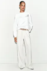 Sudadera de algodón con cuello redondo y manga larga. Presenta un diseño minimalista en color blanco con un delicado bordado de un lazo con flores en el pecho.