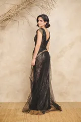 Vestido largo de tul y encaje negro con detalles dorados en los hombros y la cintura. Presenta escote en V cruzado, corte ajustado y cola de tul.