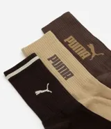 Kit de tres pares de medias deportivas Puma de caña larga. Un par es beige con dos rayas marrones y logo de Puma. Otro par es blanco liso. El tercer par es marrón oscuro con dos rayas blancas y logo de Puma. Todas están confeccionadas en algodón.