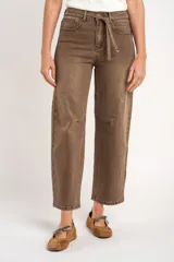 Pantalón jean de corte barrel y tiro alto, en tono marrón lavado, con bolsillos laterales y traseros, y lazo ajustable en la cintura.
