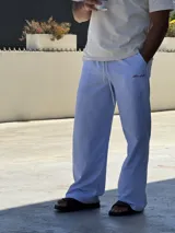 Pantalón de corte ancho y holgado, con diseño de rayas verticales finas en color azul y blanco. Presenta cintura elástica con cordón ajustable y un pequeño bordado en color rojo en la parte superior.