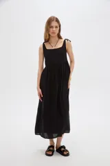 Vestido midi negro de viscosa con cuello cuadrado y tirantes finos ajustables con lazo en los hombros, de corte holgado y diseño fluido.