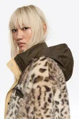 Abrigo largo reversible de corte línea A, con una cara de pelo sintético con estampado animal print y otra cara de tela técnica lisa en tono beige. Presenta capucha, cierre frontal con cremallera y botones de presión, y bolsillos laterales con cremallera.