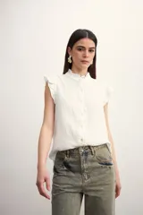 Camisa color amarillo pálido con textura arrugada, cuello mao con volados, cierre frontal con botones y mangas cortas con volados.