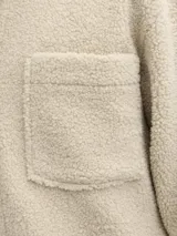 Sobrecamisa de textura teddy, color beige, con cuello camisero, cierre frontal de botones, mangas largas con puños abotonados y dos bolsillos frontales en el pecho.