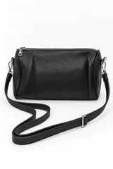 Cartera bandolera negra de formato cilíndrico, completamente cubierta de tachas plateadas en forma de corazón. Cuenta con cierre superior y correa ajustable.