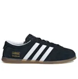 Championes Adidas modelo Gazelle Lo Pro, color negro con las tres tiras laterales en blanco y suela de goma color caramelo. Presenta el logo de la marca y el nombre del modelo en dorado en el lateral.