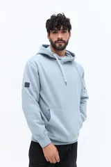 Canguro de algodón color celeste claro, con capucha ajustable mediante cordones trenzados blancos y bolsillo canguro frontal. Presenta un pequeño texto estampado en el pecho.