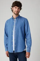Camisa de manga larga de denim azul claro, con cuello abotonado (button-down) y botones frontales blancos.