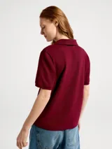 Remera tipo polo de manga corta en color bordeaux, confeccionada en tejido piqué, con cuello clásico y escote en V sin botones. Presenta un pequeño logo bordado en el pecho.