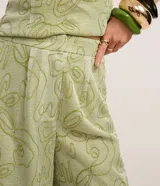 Pantalón sastre de corte recto y cintura alta, confeccionado en poliéster de color verde con bordados abstractos de líneas curvas en hilo de algodón. Presenta cierre tradicional y pliegues.