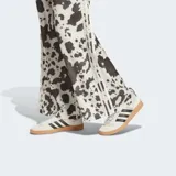 Pantalón Adidas de satén con estampado animal print tipo vaca en tonos blanco y negro, de corte holgado, perneras anchas y fluidas, cintura elástica y las icónicas 3 tiras de la marca en los laterales.