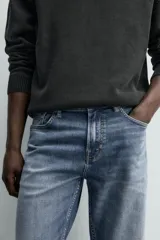Pantalón de jean corte slim fit, color gris con efecto lavado. Presenta diseño de cinco bolsillos, cierre frontal con cremallera y botón, y tejido elástico.