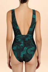 Traje de baño enterizo con escote en V profundo y detalle de aplique metálico con piedra en el centro. Presenta un diseño drapeado en la cintura y un estampado geométrico de ondas en tonos oscuros y turquesa.