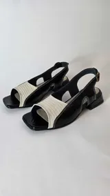 Sandalias de cuero combinadas en negro y beige, con puntera cuadrada, taco bajo y tira ajustable en el talón.