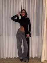 Top negro de manga larga con cuello alto y diseño asimétrico que deja al descubierto un costado del abdomen y cae en un panel largo hasta la rodilla o tobillo.