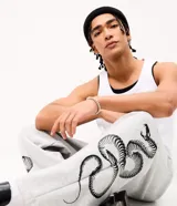 Pantalón de corte super baggy confeccionado en tejido de algodón y poliéster, color gris melange. Presenta un diseño urbano con estampado de serpiente tribal en color negro en las piernas, cintura elástica y bolsillos laterales.