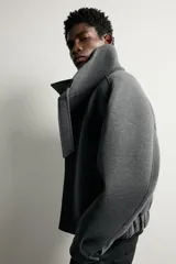 Cazadora boxy fit de tejido técnico gris oscuro, con cuello subido envolvente, cierre frontal asimétrico con cremallera oculta y bolsillos de vivo en la cadera.