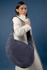 Bolso tipo bandolera de gamuza color marrón, con correa ancha ajustable decorada con tachas metálicas y cierre superior.